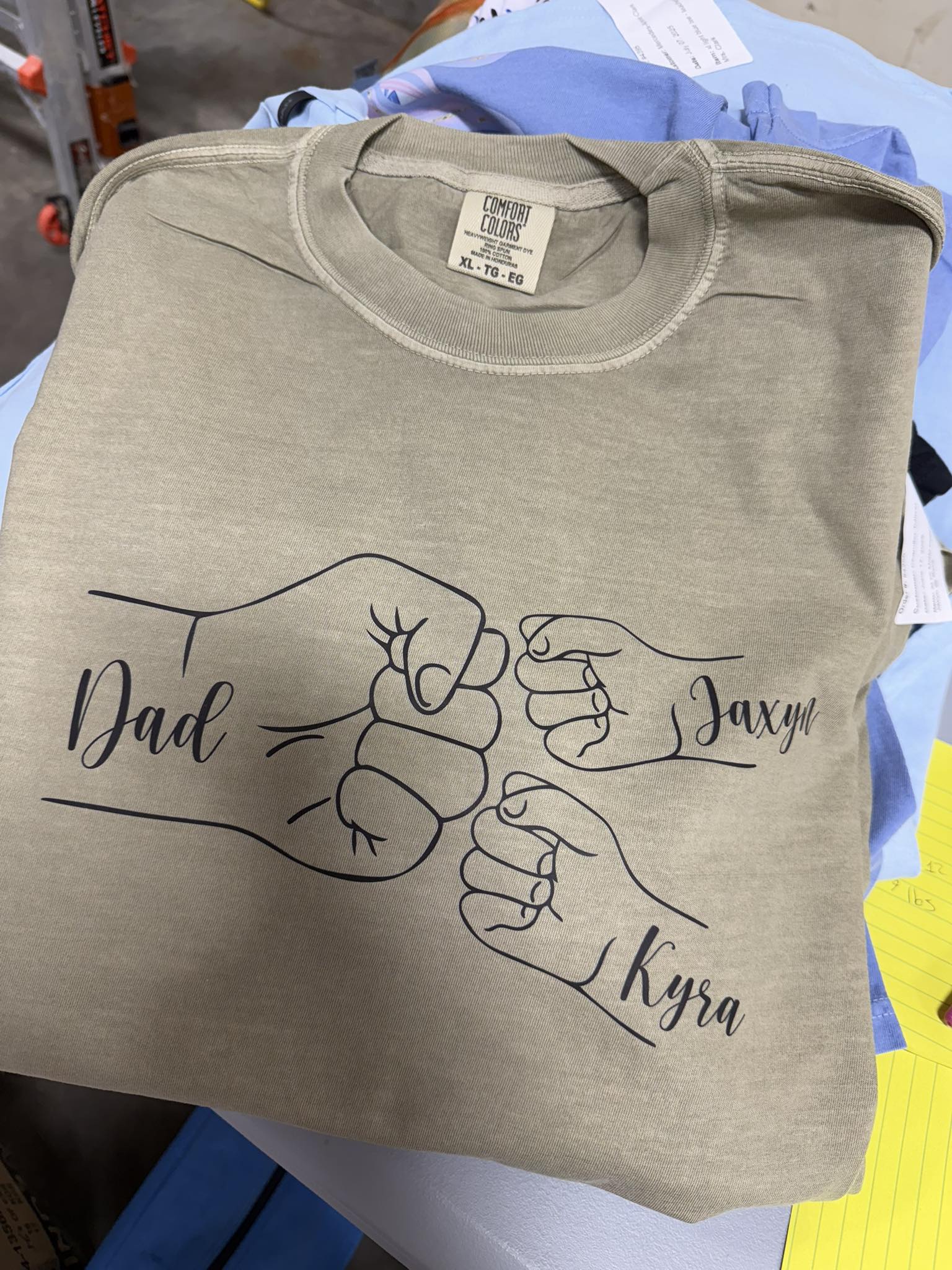 Folded beige t-shirt with graphic of two fists and names &