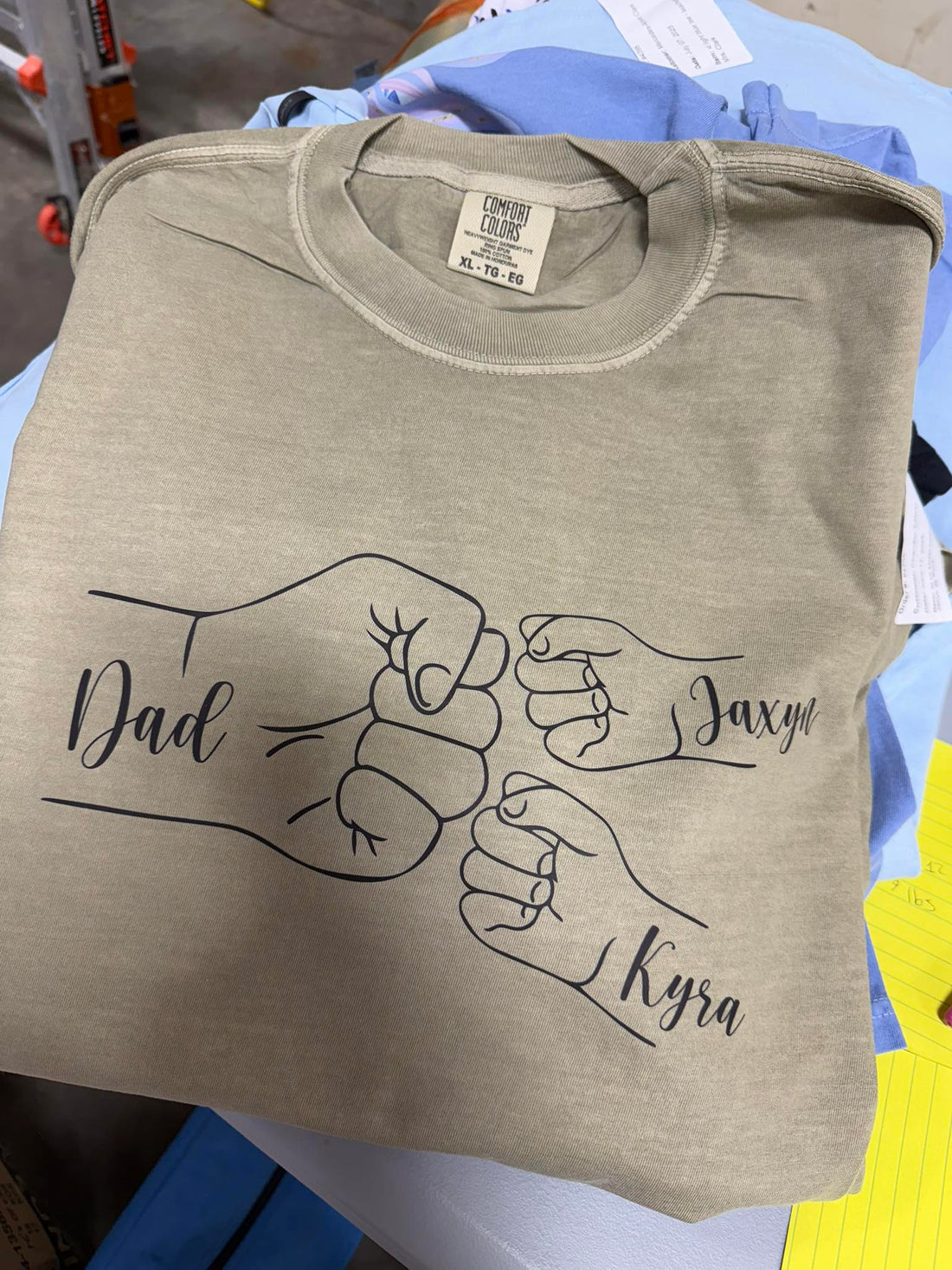 Folded beige t-shirt with graphic of two fists and names &