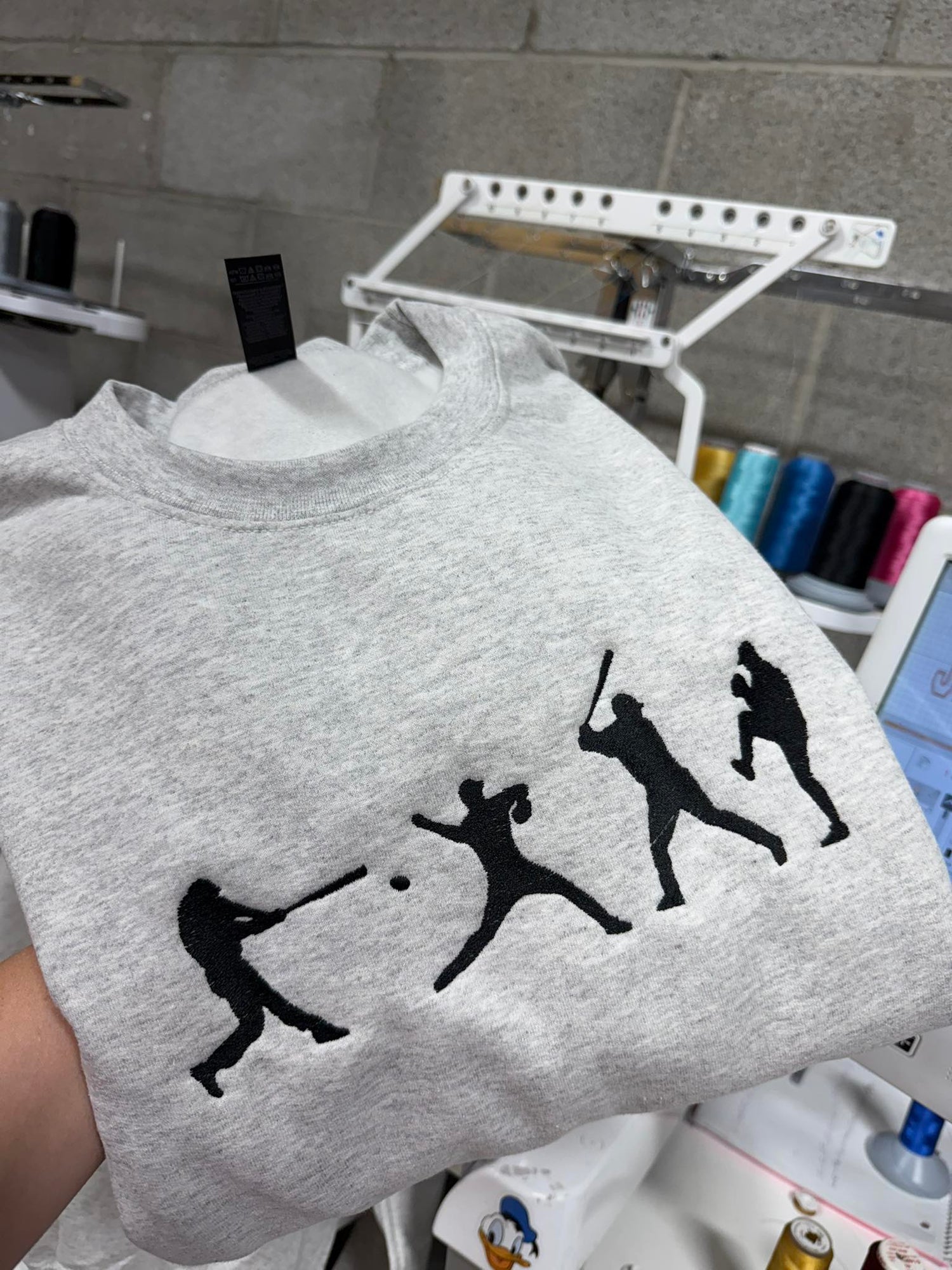 Close-up of gray crewneck sweatshirt with embroidered baseball player silhouette design