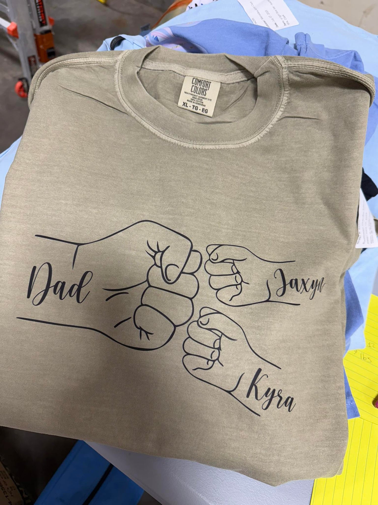 Folded beige t-shirt with graphic of two fists and names &