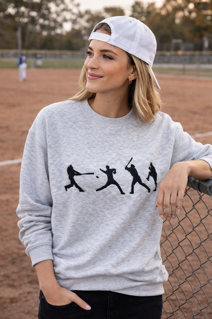 Female model wearing gray baseball crewneck sweatshirt standing at a baseball field